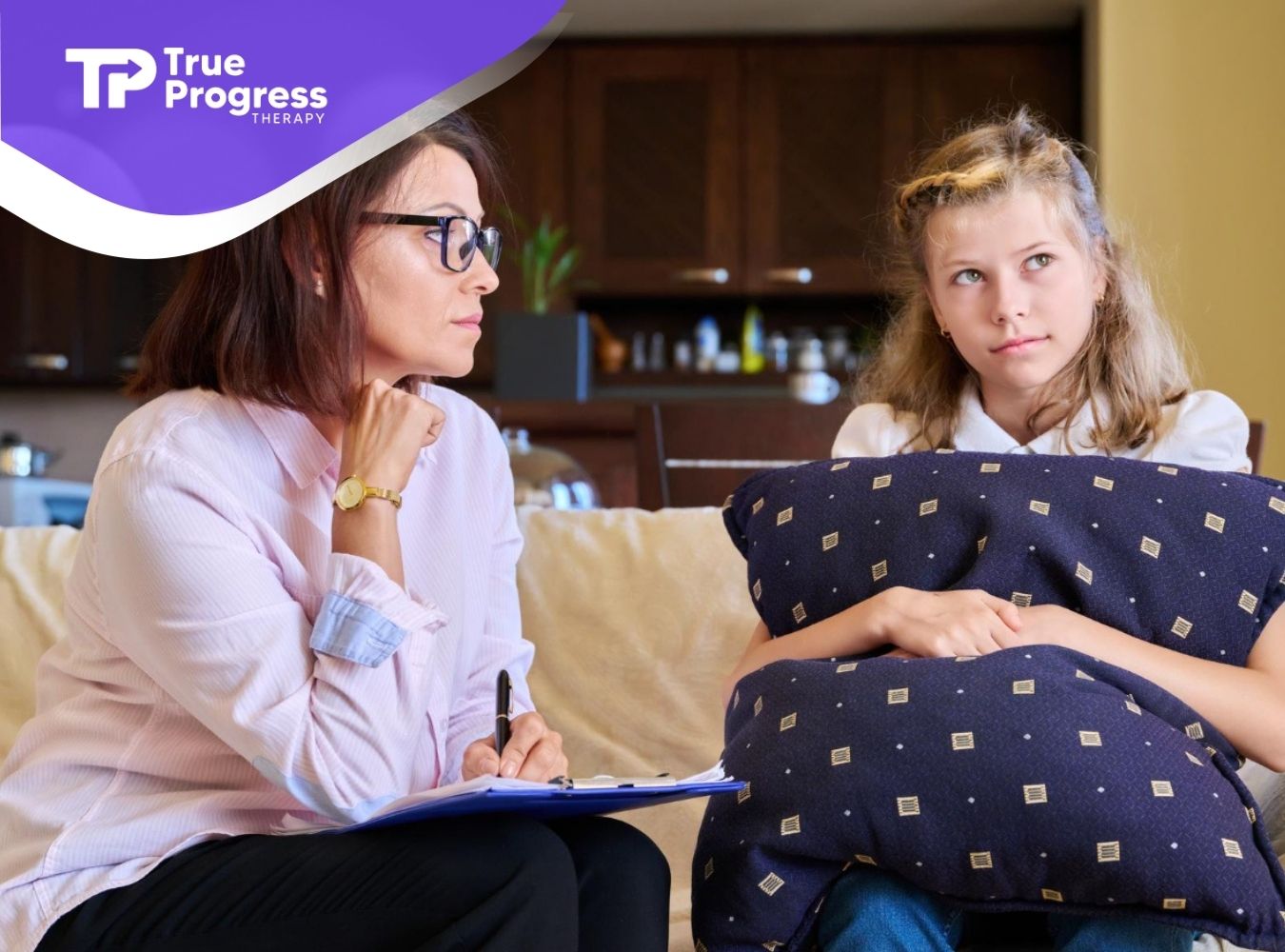ABA therapist taking notes while talking with a young girl during a therapy session.